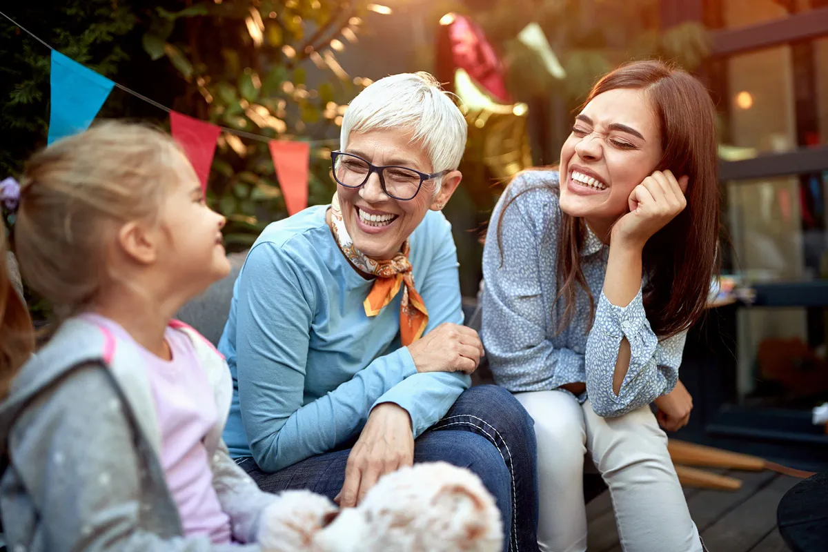 Early Signs of Dementia — Family Smiling Outdoors | Farmington Square Medford Grandmother with short gray hair laughing with daughter and granddaughter outdoors, showing family support for early signs of dementia at Farmington Square Medford.