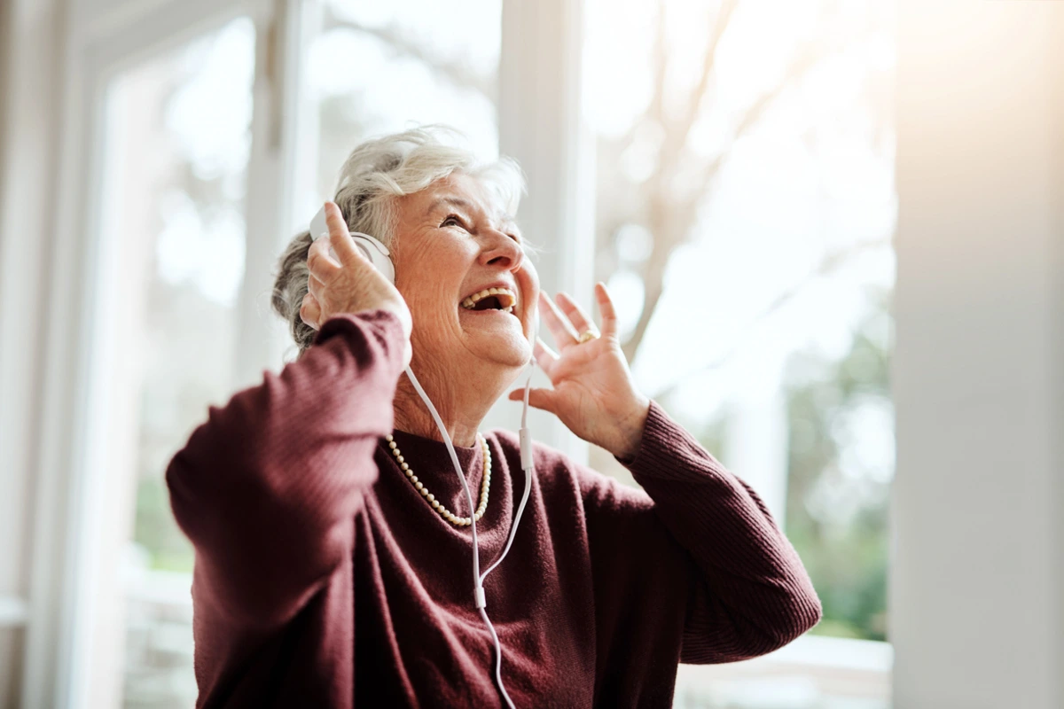 Senior woman listening to music through headphones in a peaceful memory care setting - Impact of Music Therapy