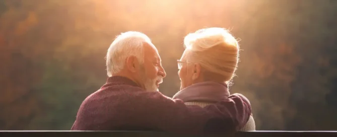 Senior couple sitting on a park bench at sunset, sharing a quiet moment and talking FAQs about sundowning.