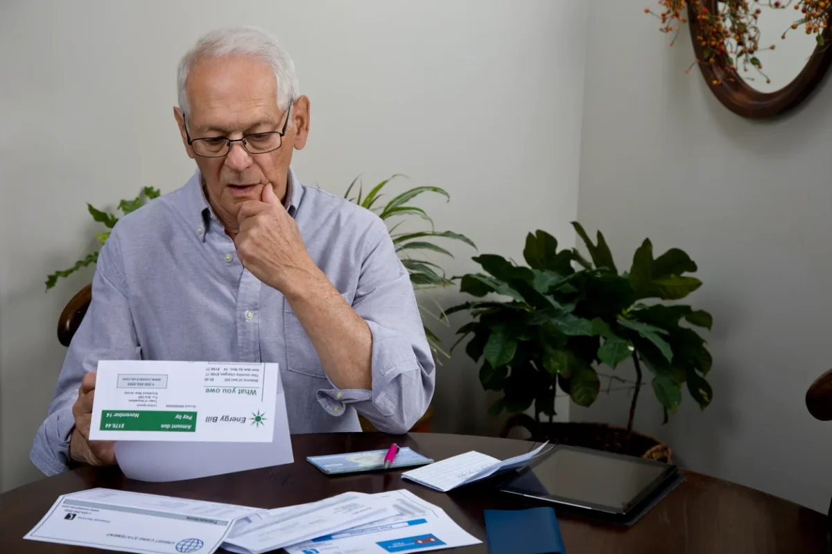 Senior man reviewing household bills at home, illustrating how trouble managing finances can be one of the early signs of dementia.